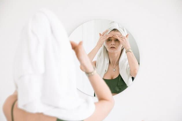 Vrouw in midlife crisis voor spiegel ziet rimpels